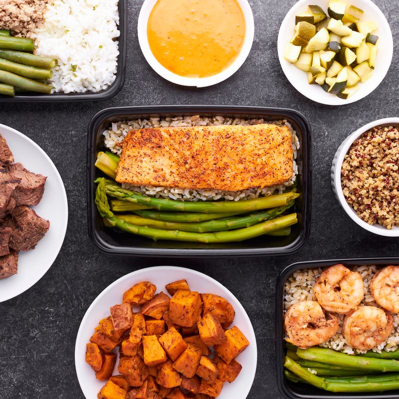 Meal prep containers with salmon, asparagus, shrimp, and sweet potatoes